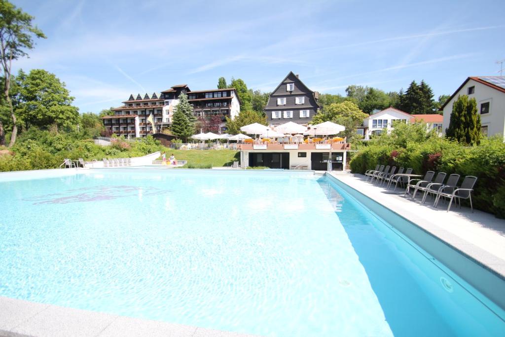 a swimming pool with chairs and a house in the background at Ringhotel Siegfriedbrunnen in Grasellenbach