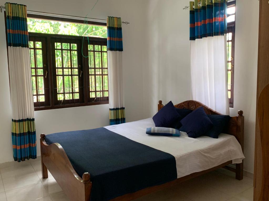 a bedroom with a bed with blue pillows and windows at Tranquil Private Villa near Bentota Beach in Bentota