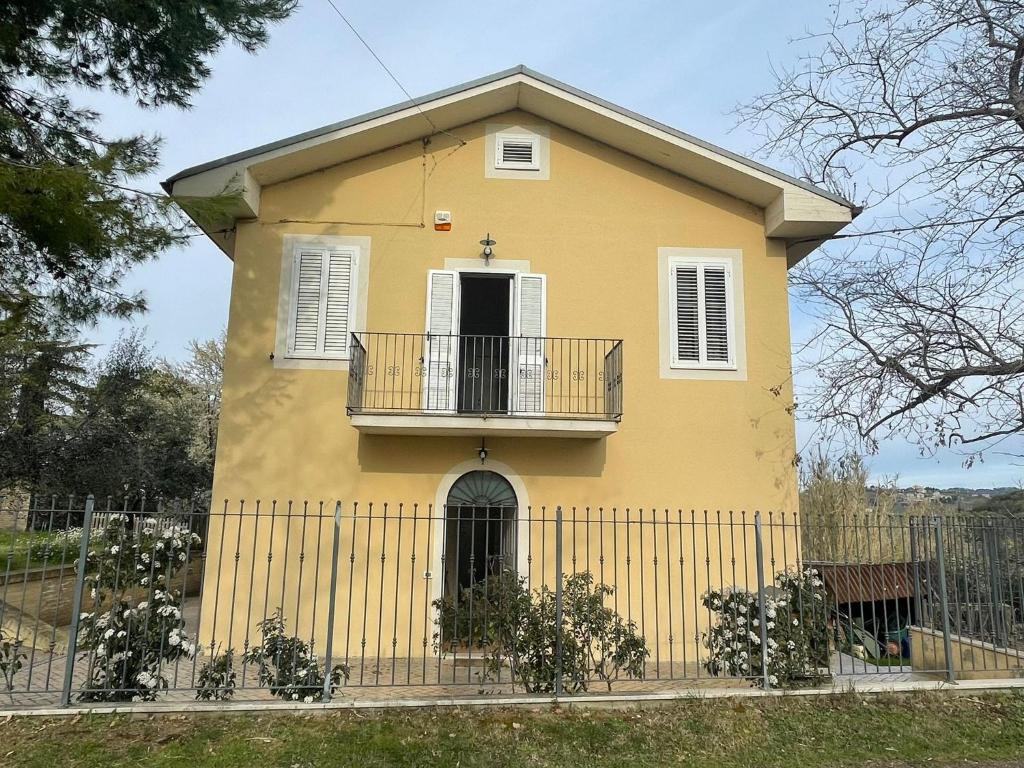 een geel huis met een balkon en een hek bij Casa Forola Holiday House in Acquaviva Picena