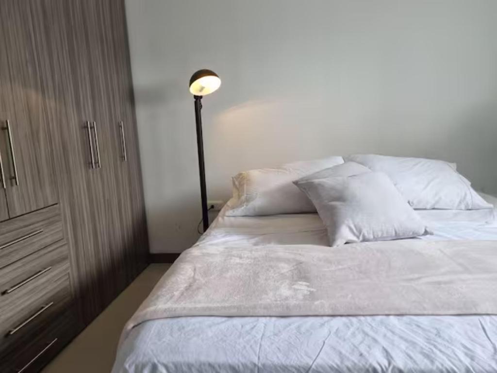uma cama com lençóis brancos e almofadas ao lado de um candeeiro em Apto Botero 1308 - WAIWA HOST em Floridablanca