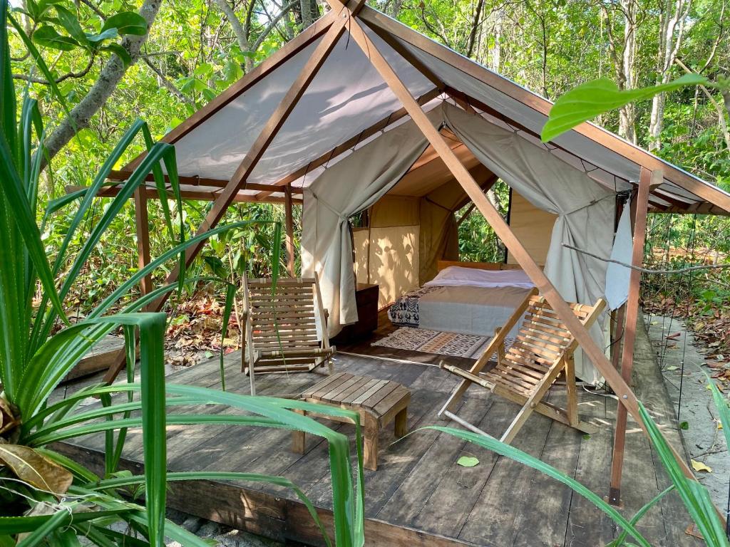 namiot z krzesłami i łóżkiem w lesie w obiekcie Camp Tarimbang w mieście Tandulujangga