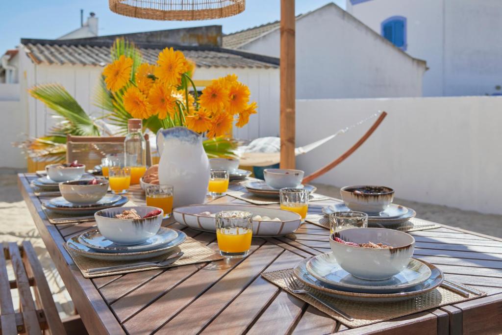 una mesa de madera con platos, tazas y flores. en Comporta Sandy Villa, By TimeCooler, en Comporta