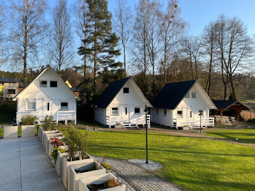 a group of white cottages in a park at Domki nad jeziorem Kazub in Cieciorka