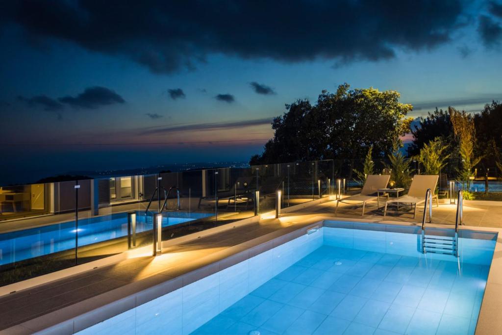 a swimming pool with lights on a house at night at Summertime Villas in Argostoli