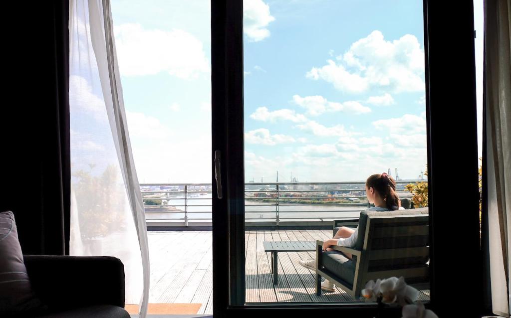 Una mujer sentada en una silla mirando por la ventana en The Suites Rainvilleterrasse, en Hamburgo