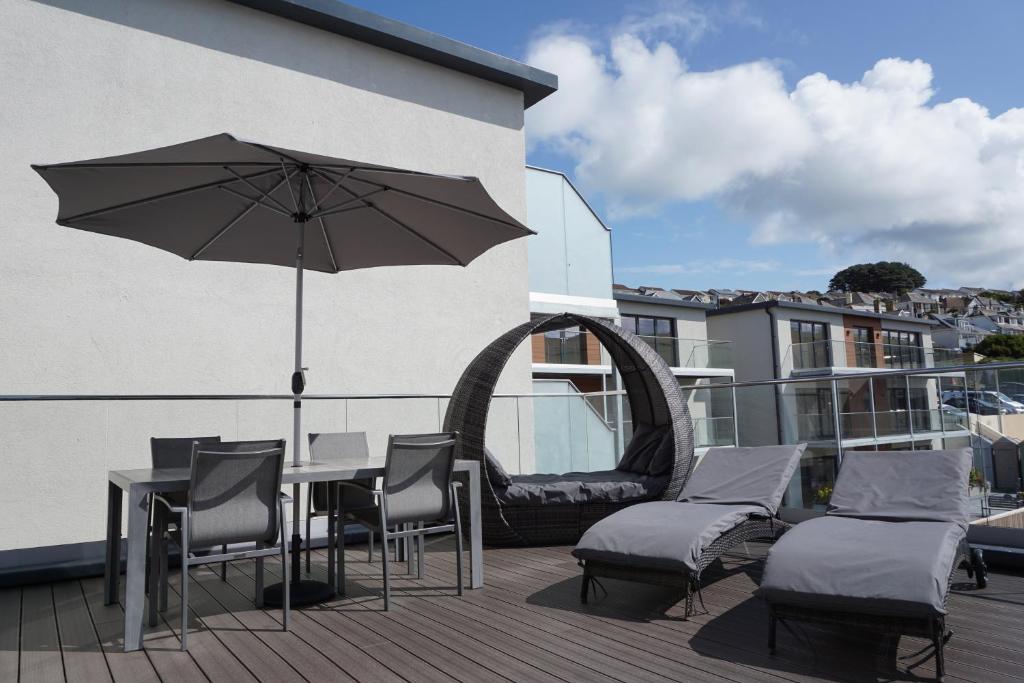 eine Terrasse mit einem Tisch, Stühlen und einem Sonnenschirm in der Unterkunft 20 Woolacombe East - Luxury Apartment at Byron Woolacombe, only 4 minute walk to Woolacombe Beach! in Woolacombe