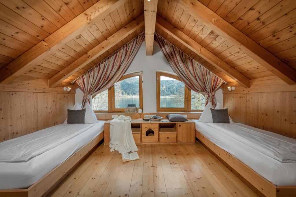 two beds in a room with wooden ceilings and windows at Seehotel Urban in Bodensdorf