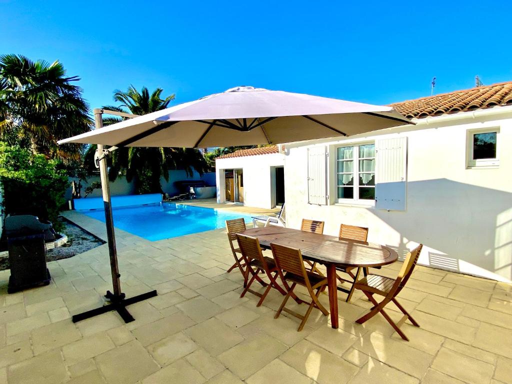 - une table et des chaises sous un parasol sur la terrasse dans l'établissement Acacias belle maison avec Piscine chauffée, Spa et Sauna, à Rivedoux-Plage