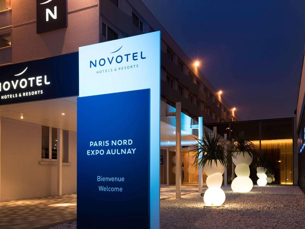 una señal frente a un edificio con luces en Novotel Paris Nord Expo Aulnay, en Aulnay-sous-Bois