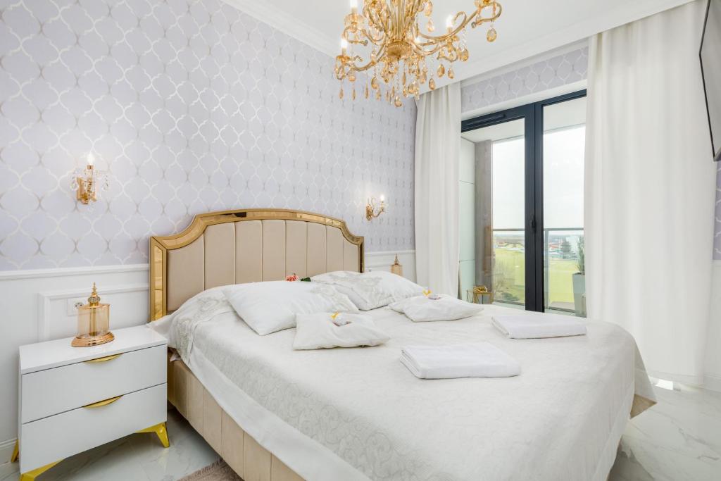 a bedroom with a bed with white sheets and a chandelier at Prestiżowe Apartamenty Natural Darłówko by Renters in Darłowo
