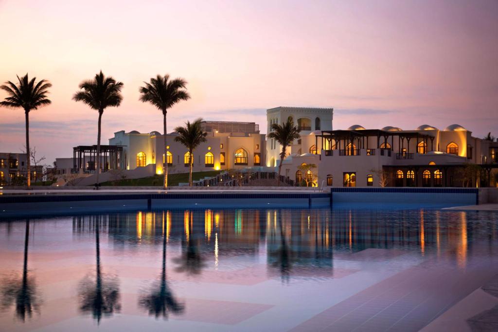 un complejo con piscina y palmeras al atardecer en Salalah Rotana Resort, en Salalah