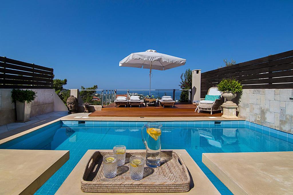 einen Pool mit einem Getränk auf einem Tablett mit einem Sonnenschirm in der Unterkunft Private pool & sea view residence in Saronida