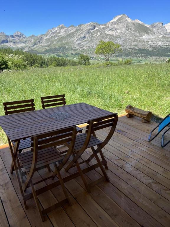 un tavolo e sedie in legno su una terrazza di legno con montagne di Appartement LA MARMOTTE DU DEVOLUY a Le Dévoluy