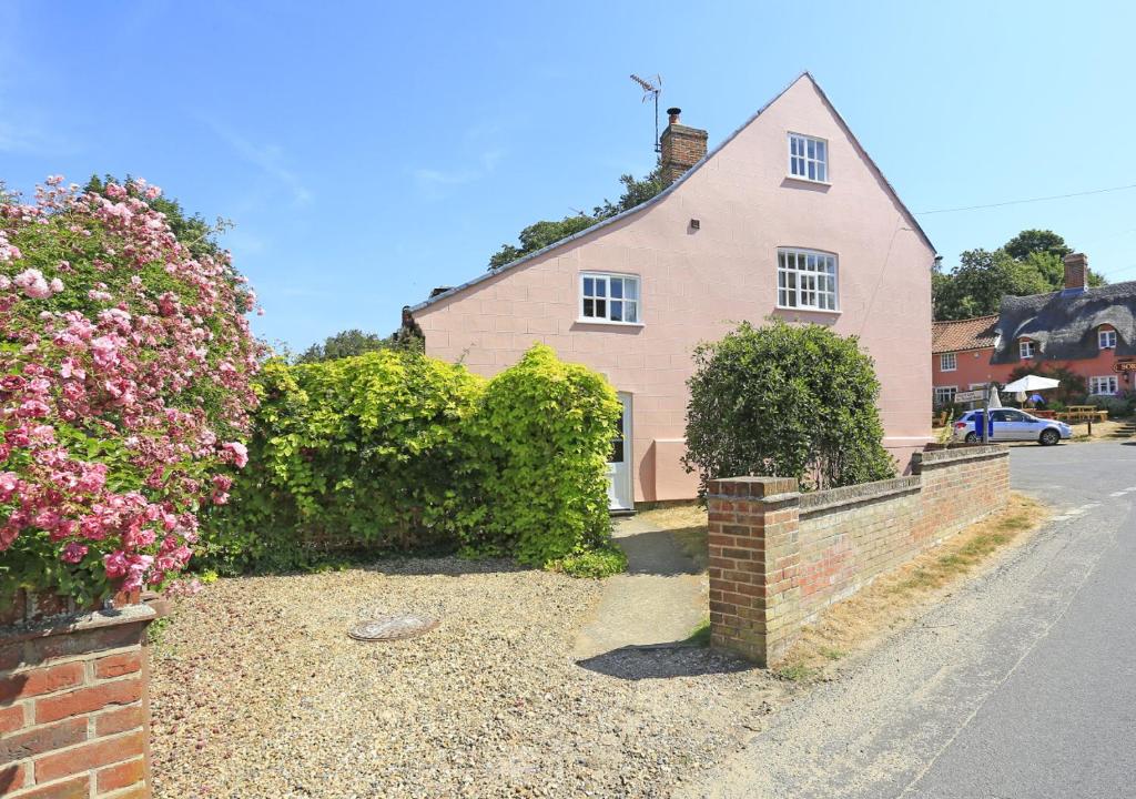 ein rosa Haus mit einem Steinzaun und Blumen in der Unterkunft 1 The Knoll in Shottisham