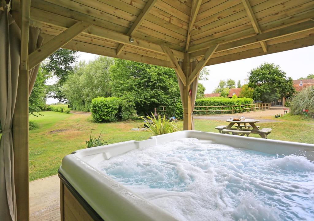 a hot tub under a wooden roof with a picnic table at Cedar in Lowestoft