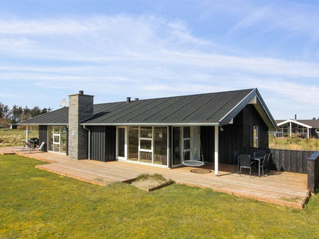 una casa con techo negro y terraza de madera en Holiday Home Segelferd - 650m from the sea in NW Jutland by Interhome, en Løkken