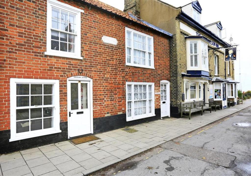 a brick building with white doors on a street at Horseshoe Cottage in Southwold