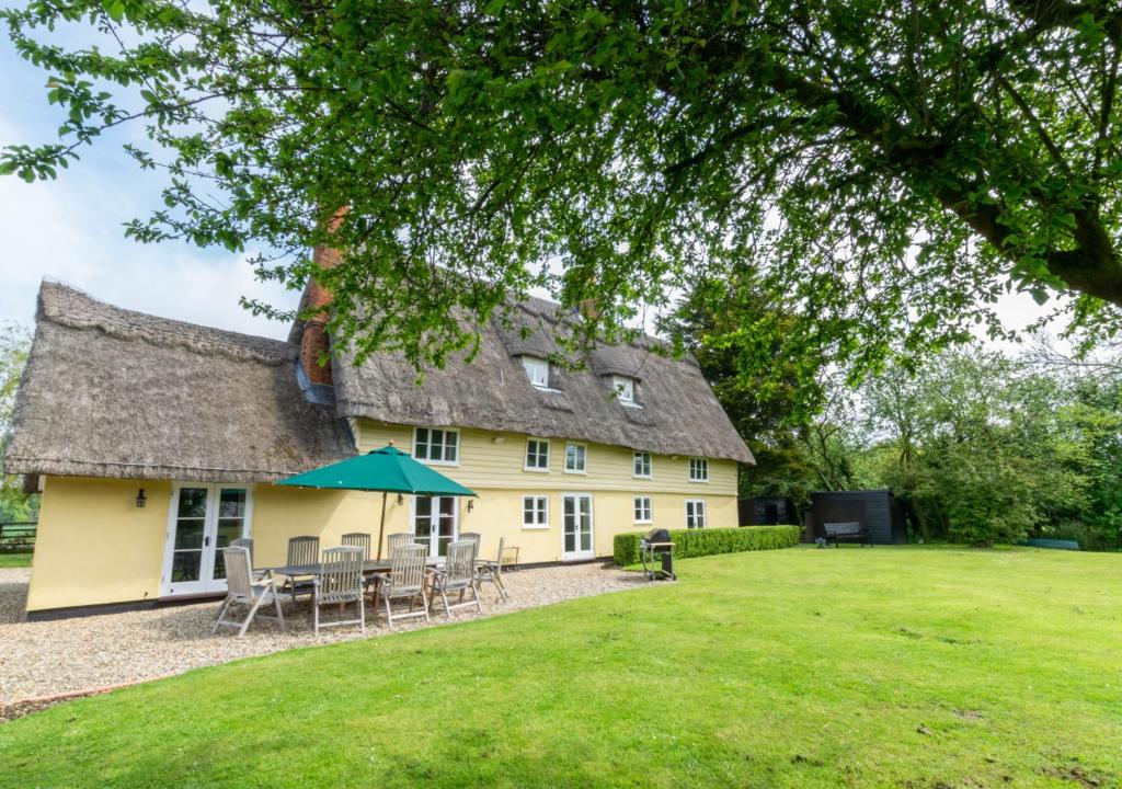 Casa amarilla con techo de paja, mesa y sillas en Old Black Horse Farm, en Finningham