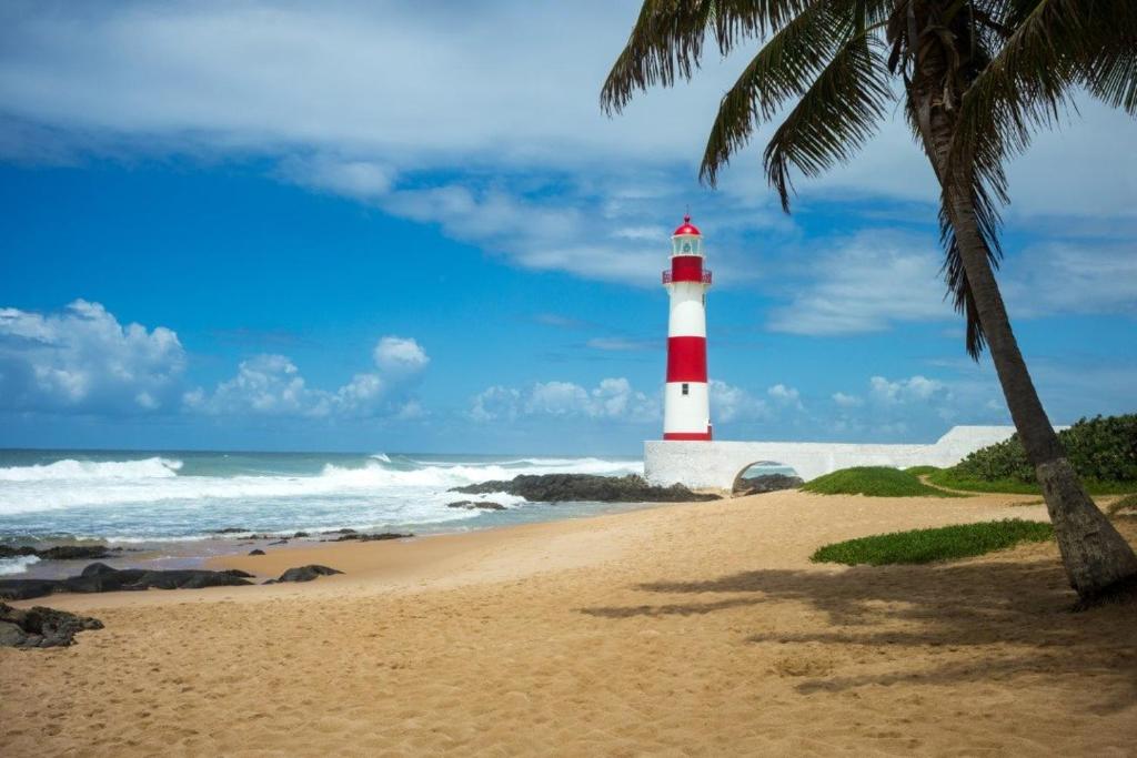 a red and white lighthouse on a beach with a palm tree at AP Itapuã in Salvador