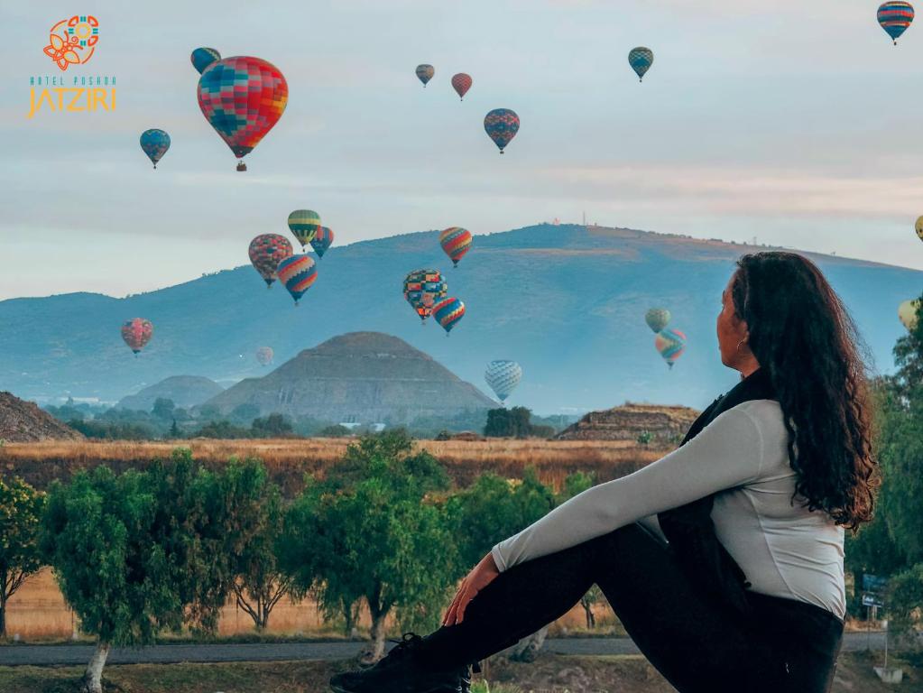 una mujer sentada en una colina mirando globos de aire caliente en Hotel Jatziri en San Juan Teotihuacan