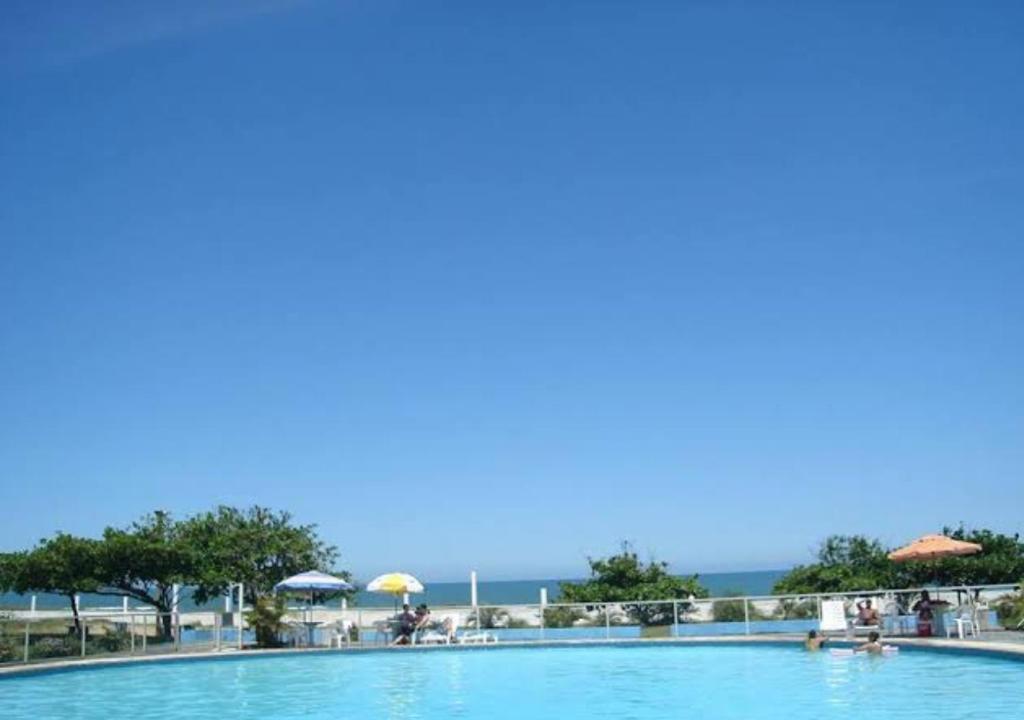 a swimming pool with umbrellas and the ocean in the background at Ervino Praia Flat in São Francisco do Sul