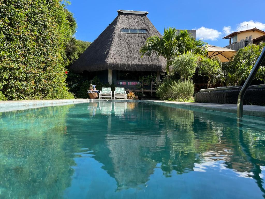 a swimming pool with two chairs and a thatched building at Oca House in Búzios