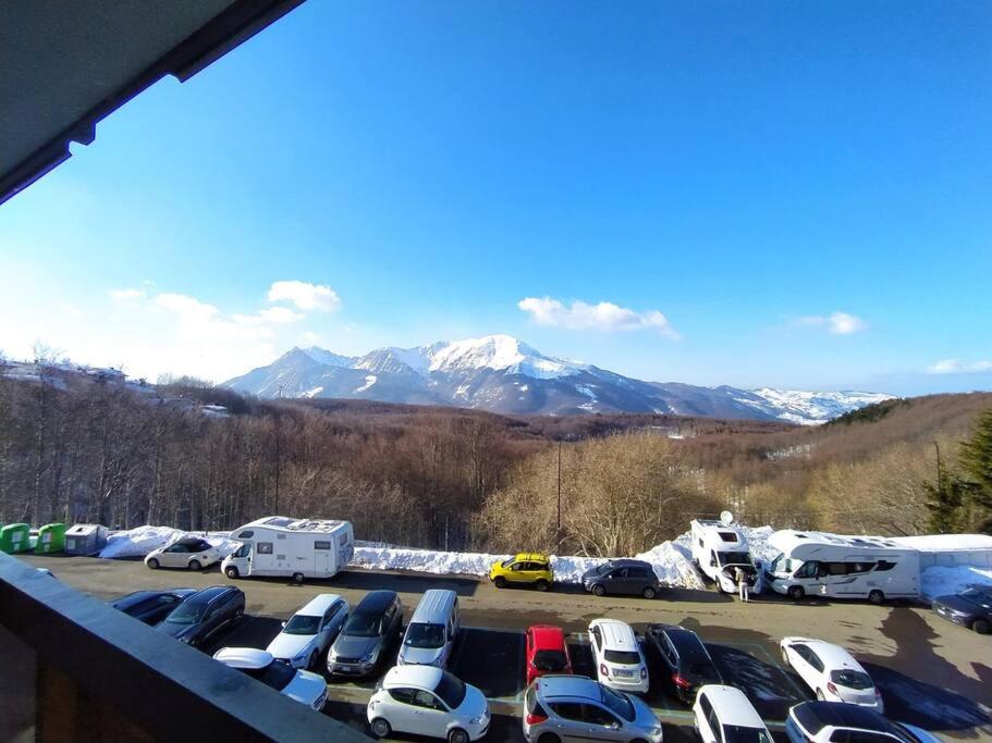 a parking lot with parked cars and snow covered mountains at Appartamento Cerreto Laghi in Cerreto Laghi