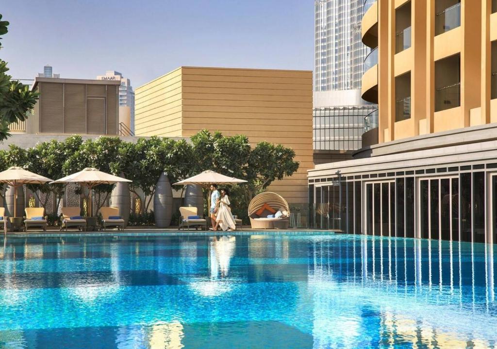 Suitestay Address Dubai Mall Residence في دبي: امرأة تمشي بجانب مسبح في مدينة