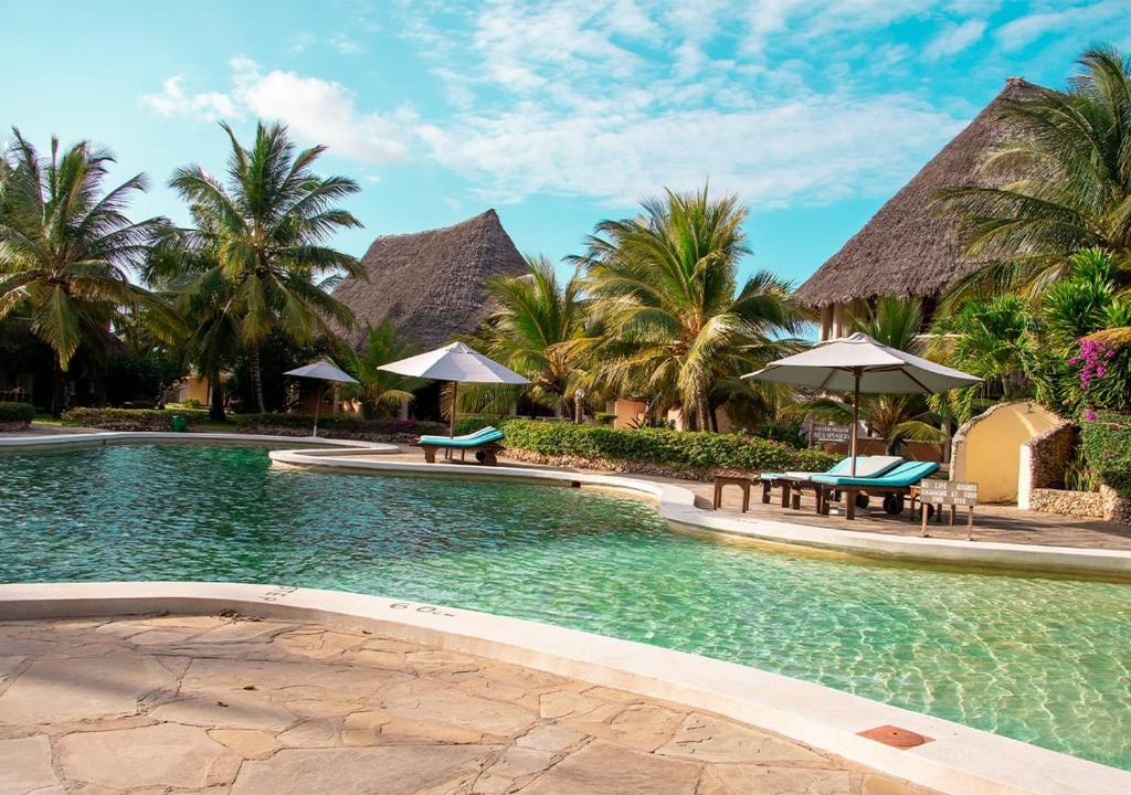 a swimming pool at a resort with tables and umbrellas at Tembo Court Apartments(2 Bdrm) in Malindi