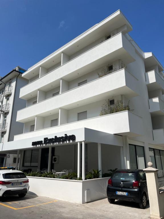 a white building with a car parked in a parking lot at Hotel Exclusive in Riccione