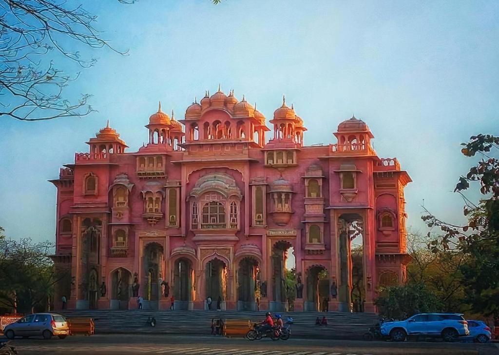 斋浦尔Click Hotel Jaipur, Raja Park的一座粉红色的建筑,前面有汽车停放