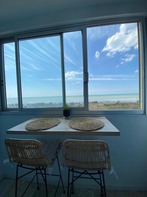 une table avec deux chaises devant une fenêtre dans l'établissement Appartement vue sur l'océan, à La Parée Preneau