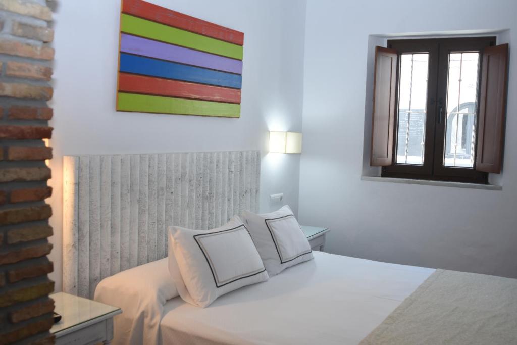 a bedroom with a white bed with a colorful painting on the wall at Hostal Doña Lola Marina in Zahara de los Atunes