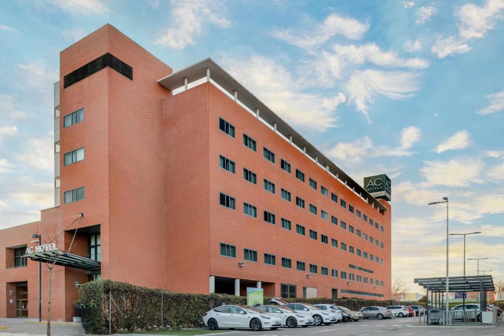 un gran edificio naranja con coches aparcados en un aparcamiento en AC Hotel Alcalá de Henares by Marriott en Alcalá de Henares