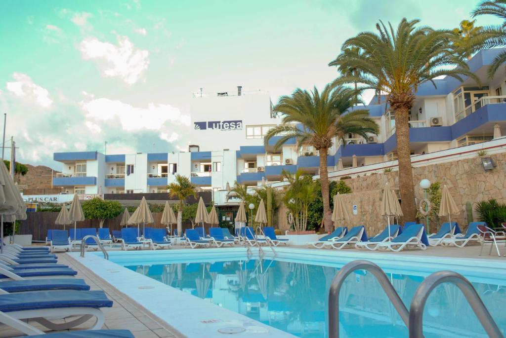 un hotel con una piscina con sillas y palmeras en Lufesa, en Puerto Rico de Gran Canaria