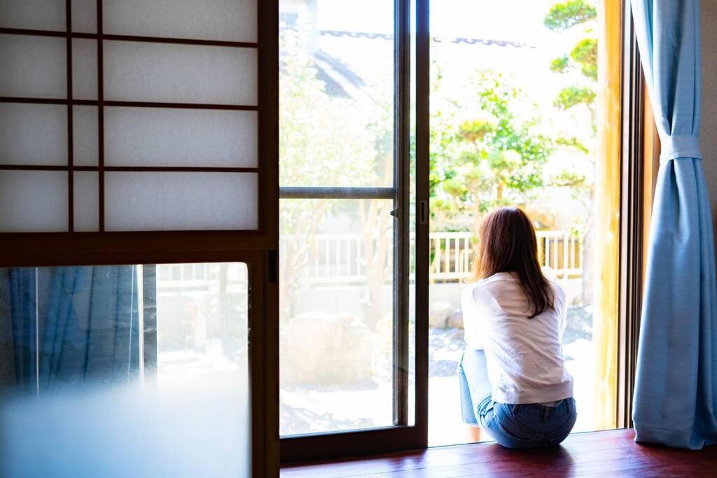 Kobieta siedząca na krześle patrząca przez okno w obiekcie 天満の宿不知火 w mieście Uki