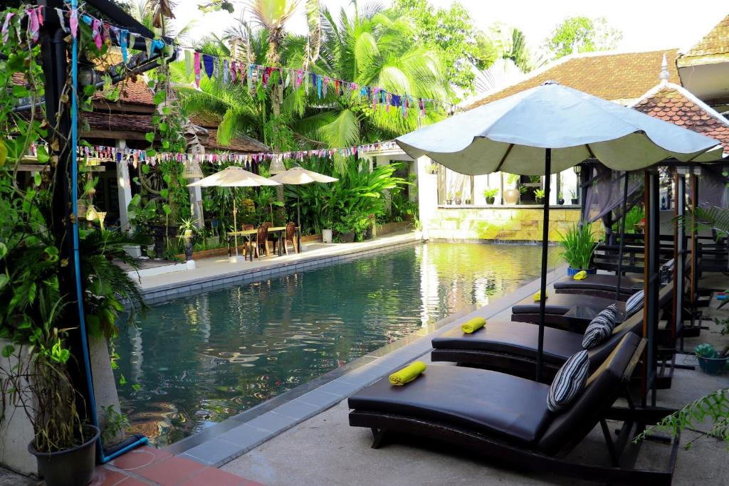 een zwembad met ligstoelen en een parasol naast een resort bij The Sanctuary Villa Battambang in Battambang