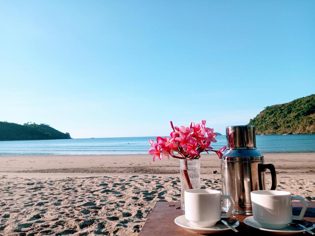 een tafel met koffiekopjes en bloemen op het strand bij Akoya Beach Sunset Camp in El Nido