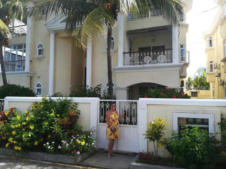 a woman standing next to a white fence in front of a building at Charming apartment about 120m from the beautiful beach of Trou aux Biches. in Trou aux Biches