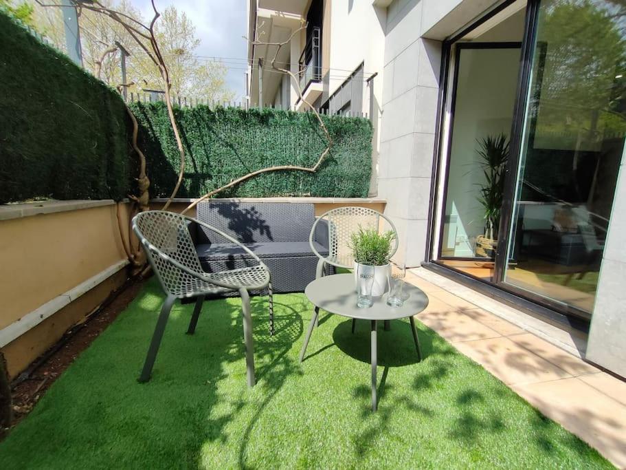 a patio with two chairs and a table on the grass at Cocon lumineux avec parking et sauna Paris direct in Asnières-sur-Seine