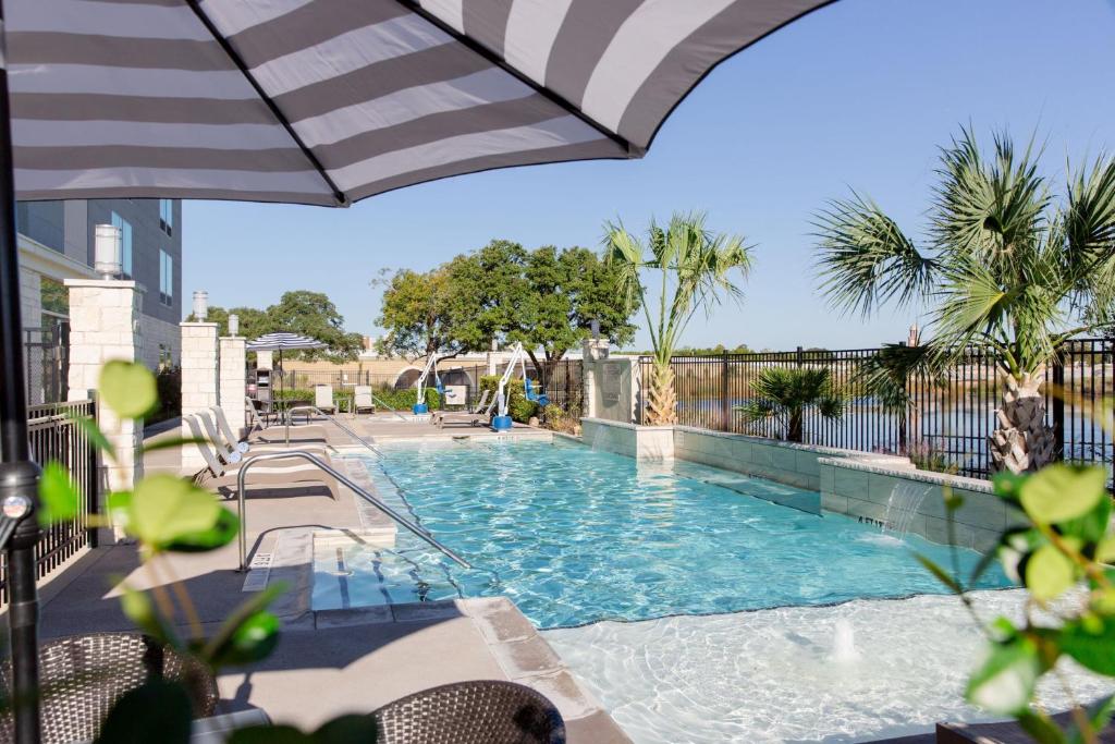 a swimming pool with an umbrella next to a building at SpringHill Suites by Marriott Austin Cedar Park in Cedar Park