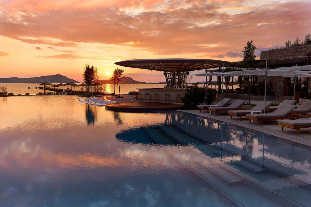 una piscina con sedie e un tramonto sullo sfondo di W Costa Navarino a Pylos