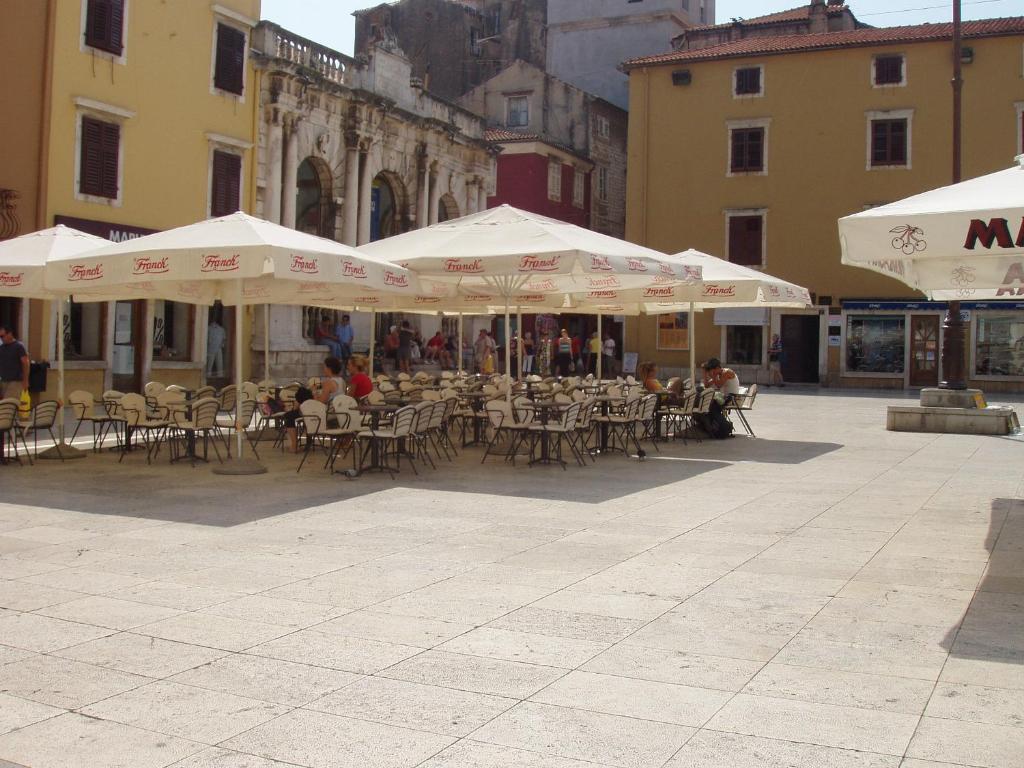 un patio al aire libre con mesas, sillas y sombrillas en Apartment Poluotok, en Zadar