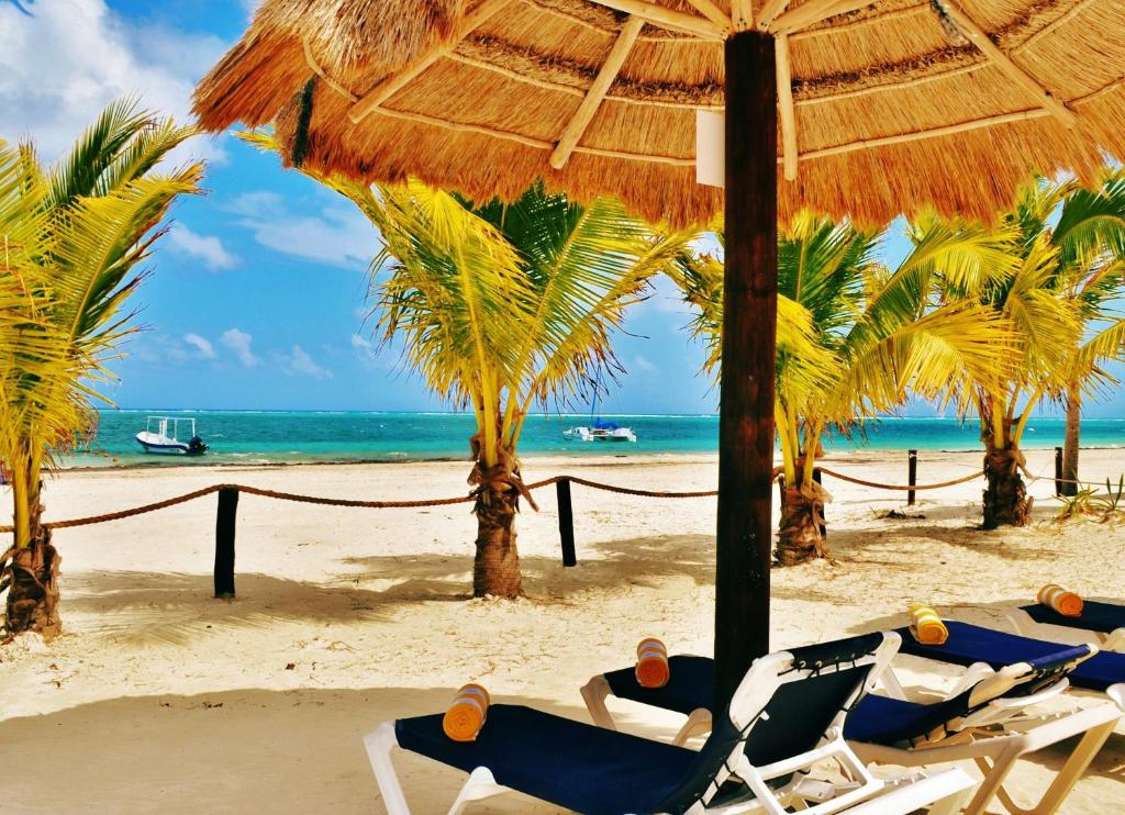 a group of people laying in chairs under an umbrella on a beach at Arrecifes Suites in Puerto Morelos