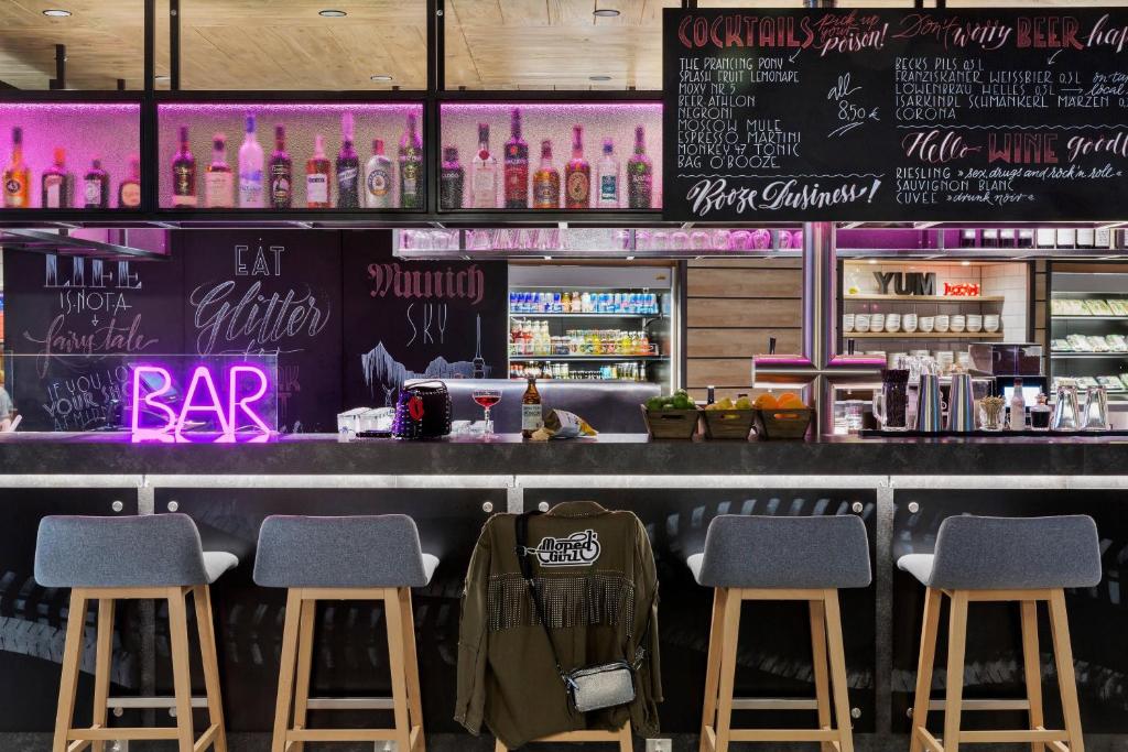 eine Bar mit drei Barhockern vor einer Theke in der Unterkunft Moxy Munich Ostbahnhof in München