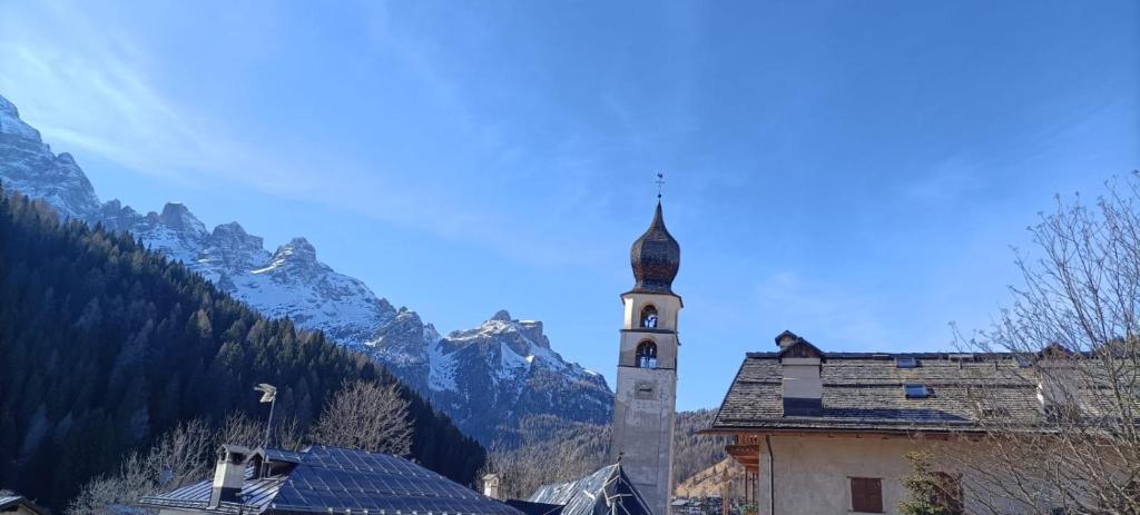 um edifício com uma torre de relógio com montanhas ao fundo em Da Carla Dolomiti Val di Zoldo em Val di Zoldo