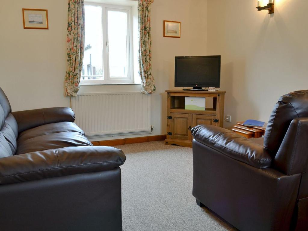 een woonkamer met 2 leren banken en een televisie bij Stable Cottage 4 - Ukc3743 in Bawdeswell