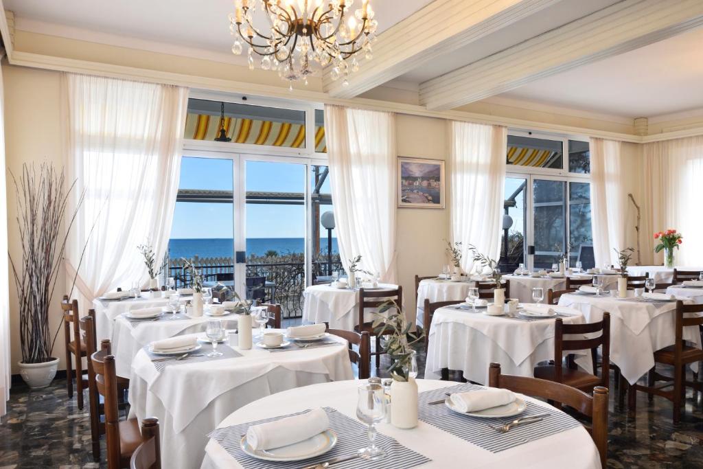 un restaurante con mesas y sillas blancas y una lámpara de araña en Hotel Villa Giulia, en Laigueglia