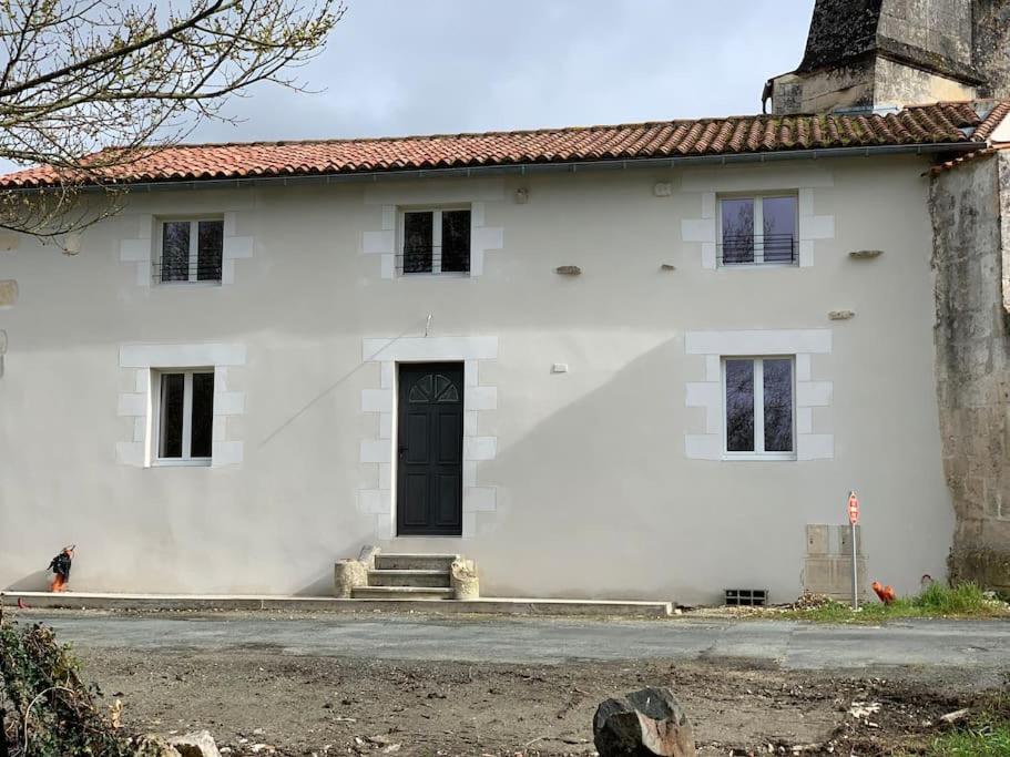 una casa blanca con una puerta negra en una calle en P’tit Gîte du prieuré, en Champdolent