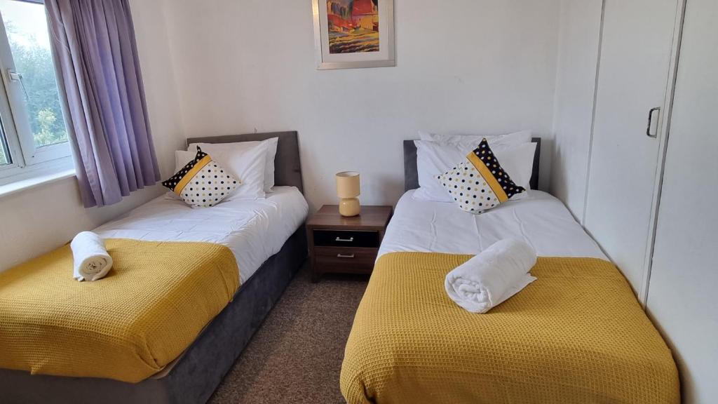 a bedroom with two beds with yellow and white sheets at RTM COMFORTABLE Home in Basildon